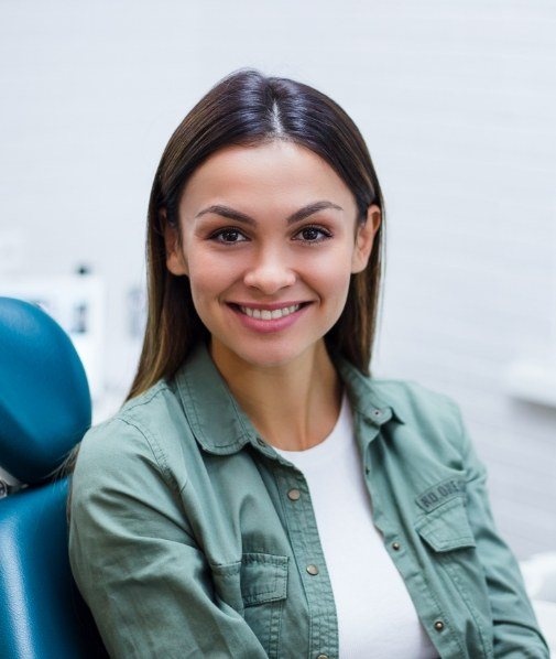 Smiling woman in green jacket sitting in dental chair