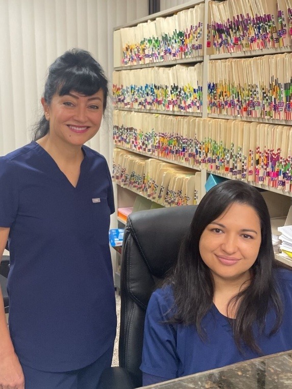 Doctor Partovi smiling next to dental team member sitting at front desk