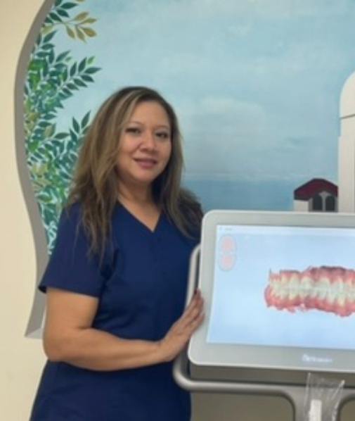 Dental team member smiling next to monitor showing digital scans of teeth